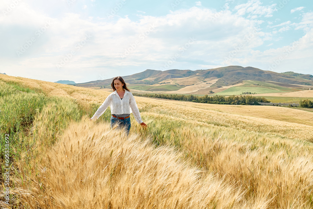 Woman walking in golden wheat field in hot summer sun and blue sky with white clouds with mountains hill landscape in background. Woman walking in golden wheat field in hot summer sun and blue sky with white clouds with mountains hill landscape in background.