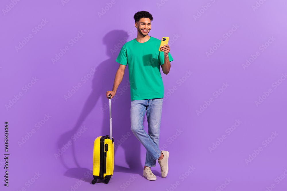 Full body photo of young man browsing phone wear stylish clothes booking hotel reservation with luggage isolated on violet color background - obrazy, fototapety, plakaty 