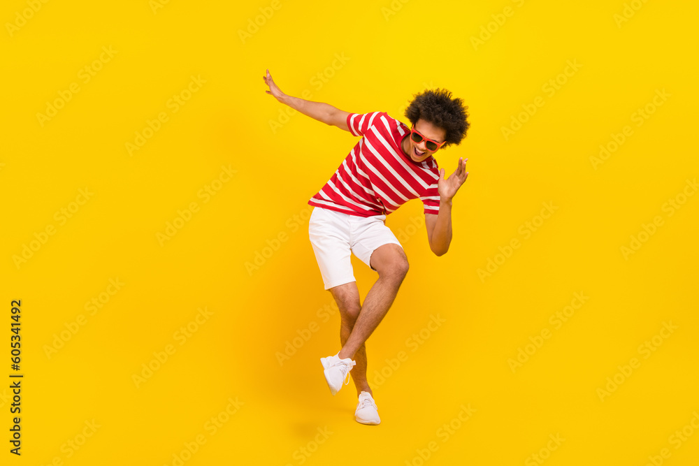 Full length photo of cool good mood man wear striped t-shirt dark spectacles dancing having fun isolated yellow color background Full length photo of cool good mood man wear striped t-shirt dark spectacles dancing having fun isolated yellow color background