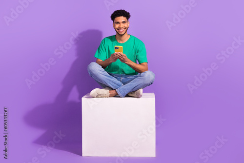 Full body photo of youth man enjoy his modern samsung smartphone four digital cameras sitting podium isolated on violet color background