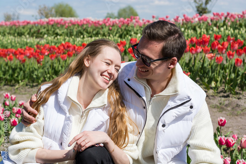 Young beautiful smiling couple on the background of a field of colorful tulips.