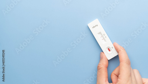 Hand holding Hepatitis B Virus Surface Antigen Test Kit with positive result on blue background. Screening for hepatitis B uses a blood sample, collected from a finger prick. World hepatitis day. photo