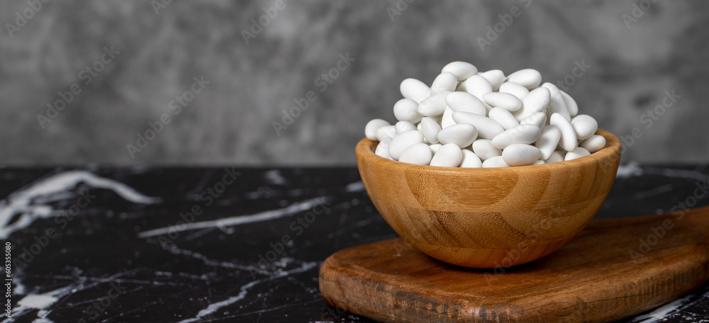 Almond candy. Sugar coated almond candy in wooden bowl on dark background. Small multi-colored candies. Copy space. Empty space for text Almond candy. Sugar coated almond candy in wooden bowl on dark background. Small multi-colored candies. Copy space. Empty space for text
