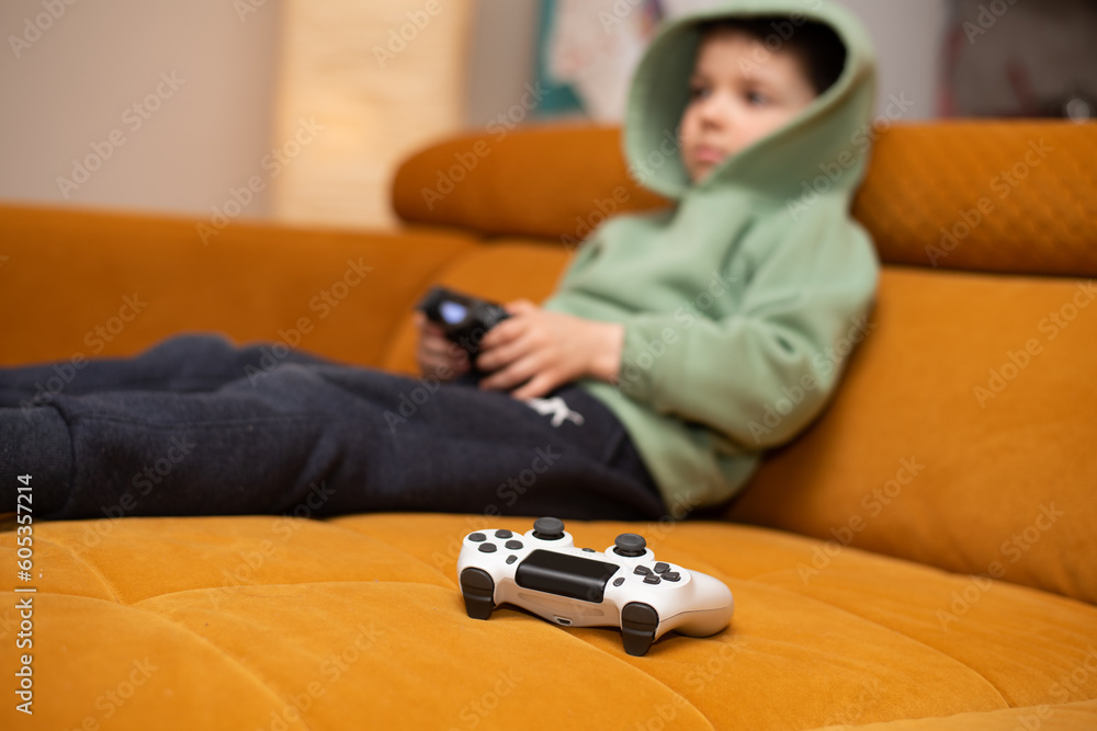 Cute 5 year old boy playing video game console while sitting on orange couch at home. Cute 5 year old boy playing video game console while sitting on orange couch at home.