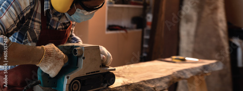 фотографія Carpenter use a hand-held electric sanding machine belt sander to level surface wood in carpentry workshop