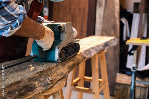 Using sanding machine belt sander to level surface wood. Carpenter use a hand-held electric sanding machine in carpentry workshop. Close-up and selective soft focus for movement feeling on machine