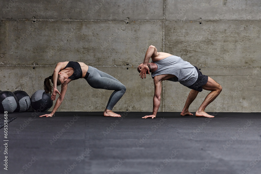 Fototapeta premium An attractive couple in the gym engaging in various stretching exercises together, showcasing their dedication to fitness, flexibility, and overall well-being. With synchronized movements, they