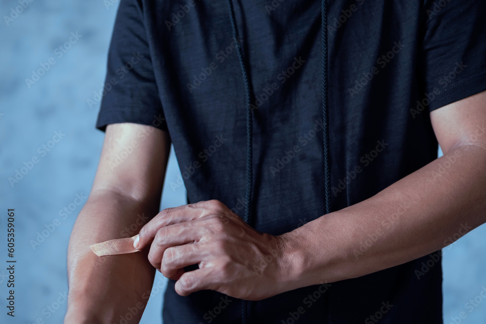 A man putting a plaster on his arm against an abstract light blue background A man putting a plaster on his arm against an abstract light blue background