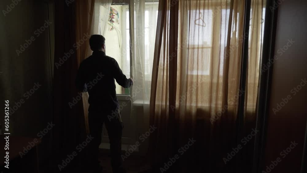 The silhouette of a man standing at the window and talking on a mobile phone. The silhouette of a man standing at the window and talking on a mobile phone.