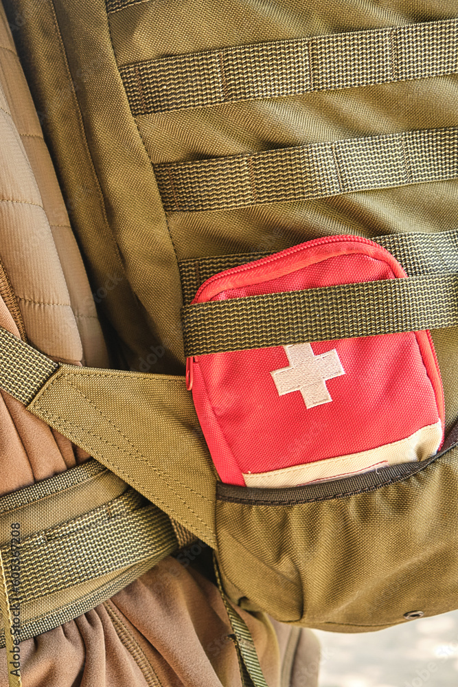 Naklejka premium A red first aid kit with a white cross in the pocket of a tactical military olive backpack with a Molle system