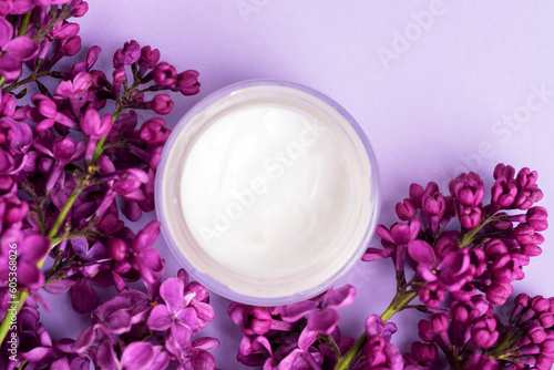 Cream jar and lilac flowers on light purple background. Natural cosmetics  skin care concept. Top view  flat lay
