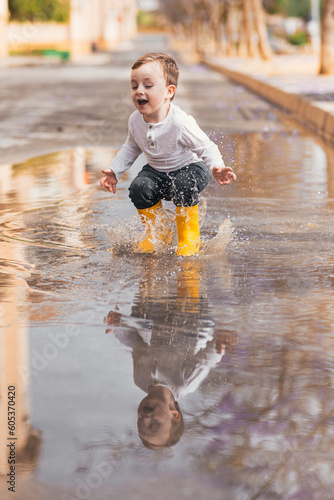 boy in yellow rubber boots jumping over a puddle in the rain