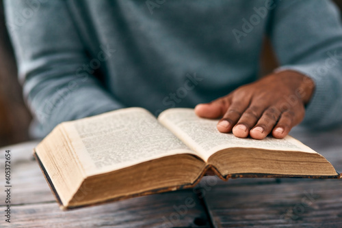 Hands, faith and a man reading the bible at a table outdoor in the park for religion or belief in god. Book, story and spiritual with a male christian sitting in the garden for study or worship