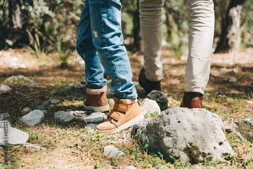 Close-up view of tourists school boy and his dad feet walking a stone footpath in spring forest. Child boy and father wearing hiking boots while walking in summer greenwood forest.