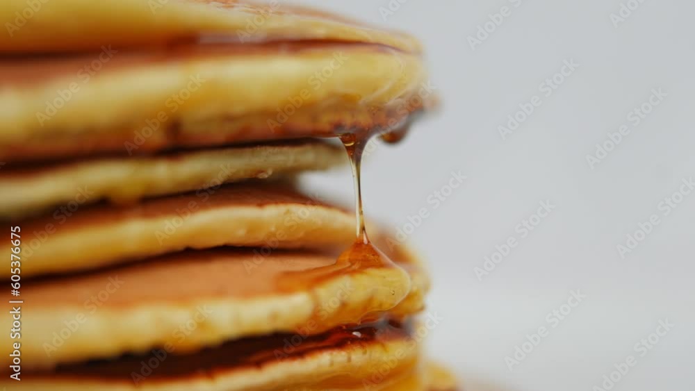 Closeup honey drops falling on side of pile of crepes in slow motion
