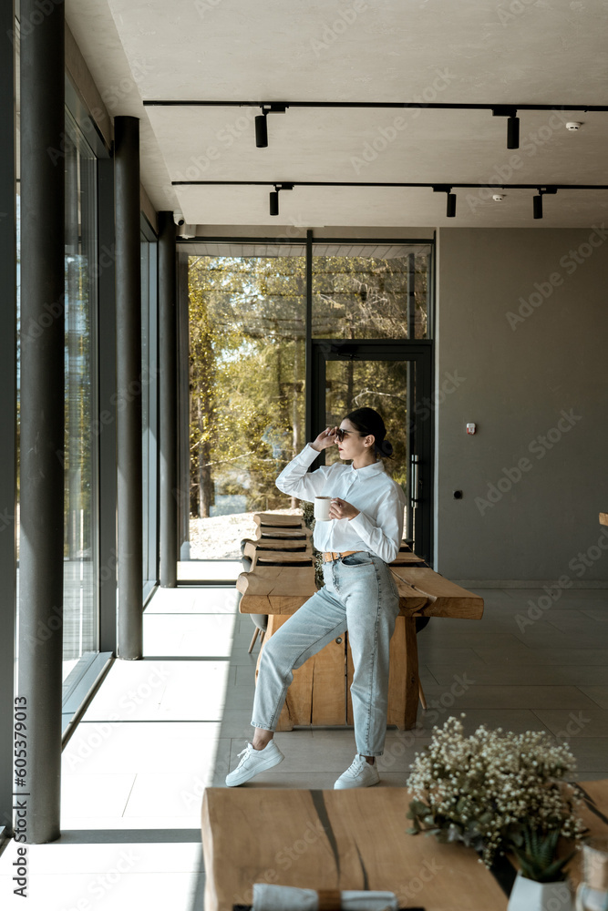Pretty woman in a white shirt and glasses posing against the backdrop of a modern mountain hotel.Businessman woman concept