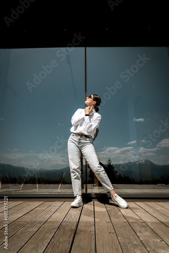 Pretty woman in a white shirt and glasses posing against the backdrop of a modern mountain hotel.Businessman woman concept