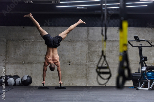 Fototapeta Naklejka Na Ścianę i Meble -  A muscular man in a handstand position, showcasing his exceptional balance and body control while performing a variety of exercises to enhance his overall body stability and strength in a modern gym