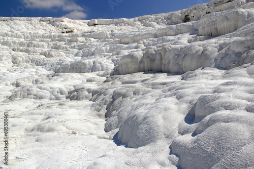 Close-up photo of snow-white travertine without people against a bright blue sky with clouds in Pamukkale  Turkey