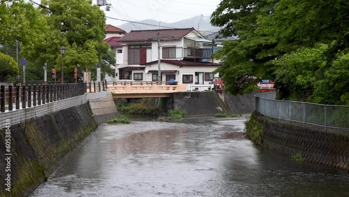 Water flows down river under bridge with cyclist and car on rainy day in Japan photo