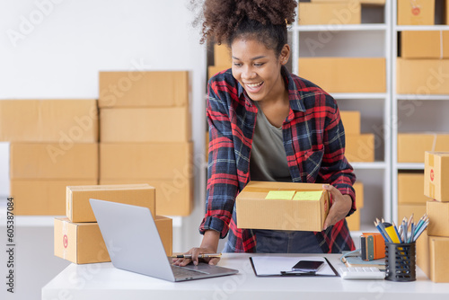 African American female fashion seller using computer checking ecommerce clothing store orders.young business woman entrepreneur working on laptop preparing SME online shipping delivery parcels boxes.