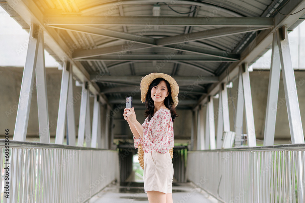 young asian woman traveler with weaving basket using mobile phone and standing on overpass. Journey trip lifestyle, world travel explorer or Asia summer tourism concept.