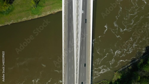 Cars drive on massive Redzinski Bridge over river with dark green water flowing near Wroclaw. Cable-stayed bridge above green island vertical aerial motion photo