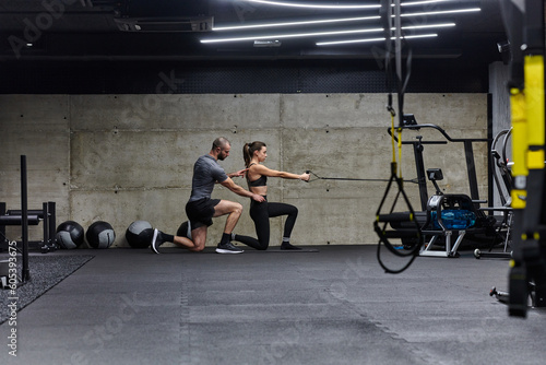 A muscular man assisting a fit woman in a modern gym as they engage in various body exercises and muscle stretches, showcasing their dedication to fitness and benefiting from teamwork and support