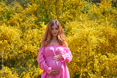 Happy pregnant woman in a yellow flowers field. Pregnancy, maternity, preparation and expectation concept.Pregnant woman in pink dress holds hands on belly outdoor. 