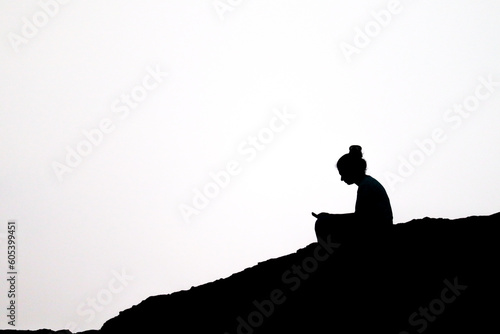 the black and white silhouette image of a sad young girl sitting near mountain