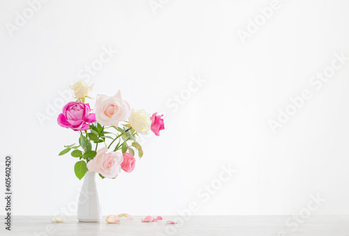 pink and white roses in white ceramic vase on white background © Maya Kruchancova