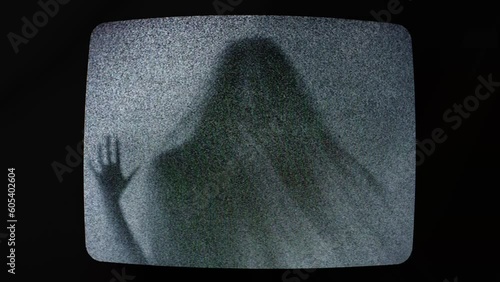 The ominous scary silhouette of a veiled ghost trapped inside an old retro analog television, touching the screen, struggling to escape, mixed with static noise.
