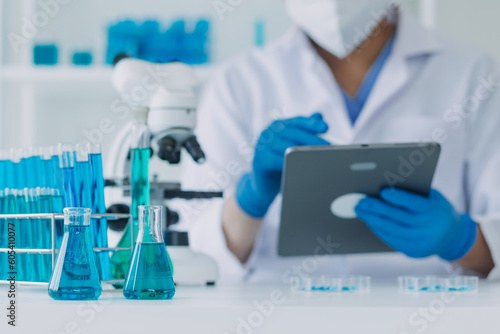 medical or scientific researcher researching and experimenting Multi-colored solution  vial and microscope In the laboratory or in the laboratory by wearing blue gloves and white clothing completely.