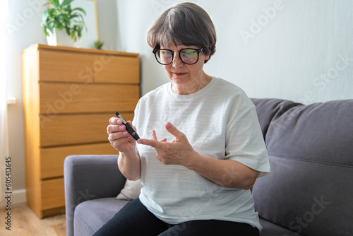 Elderly woman sit on sofa in morning holding glucose meter lancet needles pricks skin obtain blood sample, diabetic patient easily do check up control of blood sugar levels at home, diabetes concept photo