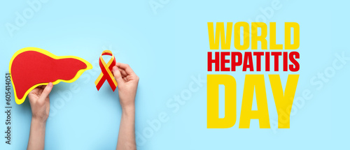 Hands with awareness ribbon and paper liver on light blue background. World Hepatitis Day