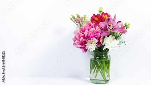 Bouquet of various natural flowers in a glass jar on a white background.
