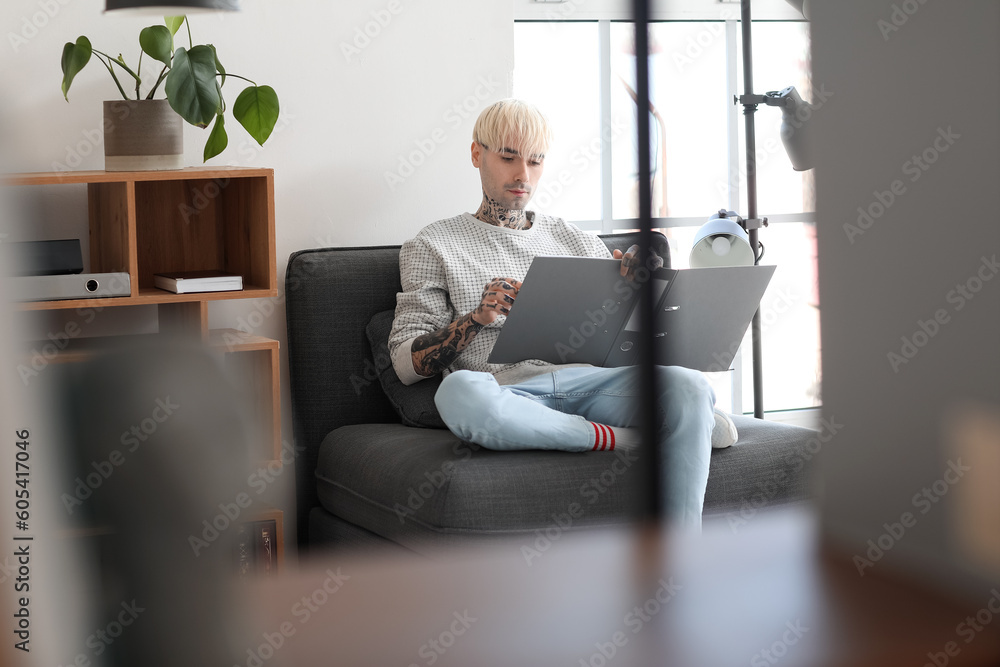 Young tattooed man with folder sitting in office Young tattooed man with folder sitting in office