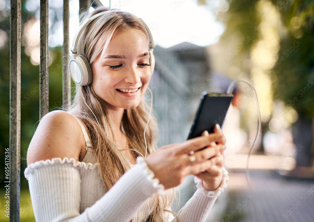 Cheerful teenager student girl sitting and listening to music with headphones from a smart phone