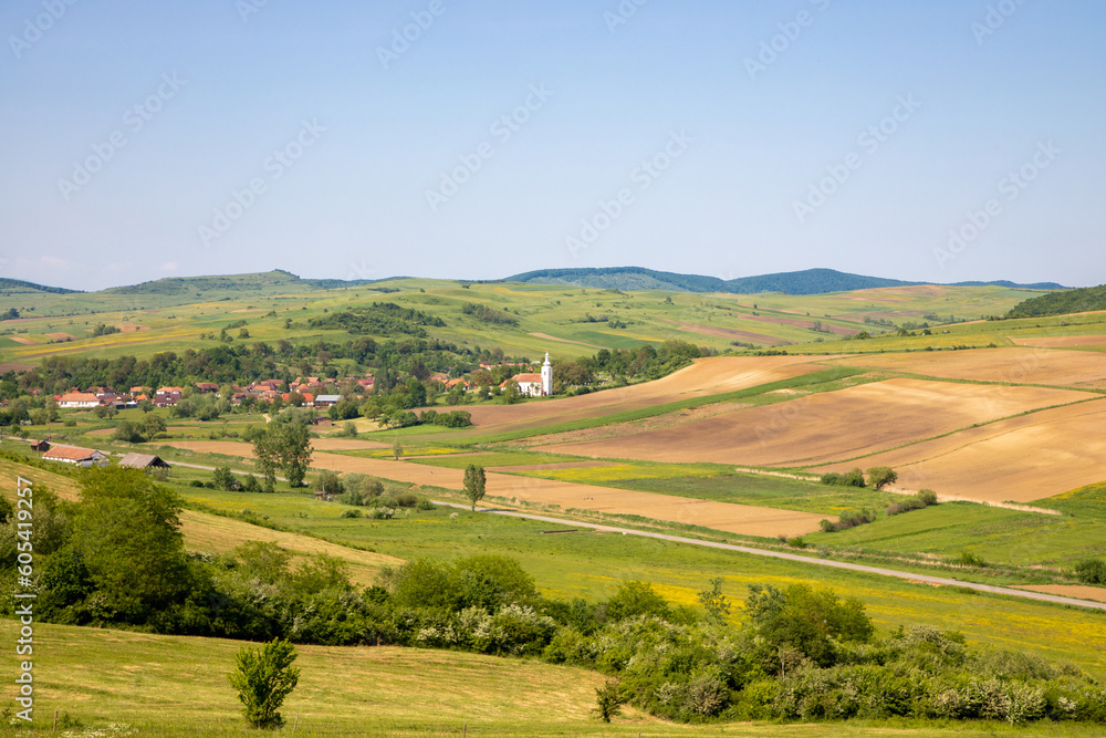 Small szekler village among green hills, blue sky in the spring. East European villages - Transylvania region