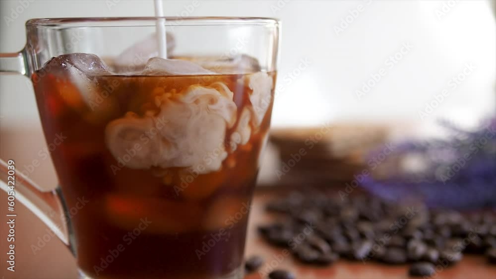 Ice coffee in a tall glass and pouring milk slowmotion shot.Cold summer drink. glass of ice and coffee beans on a table, Cookies and milk bottle on background Ice coffee in a tall glass and pouring milk slowmotion shot.Cold summer drink. glass of ice and coffee beans on a table, Cookies and milk bottle on background