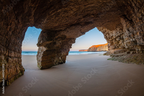 Large cave in the coastal cliffs at a beach (Praia do Beliche) of the Algarve at sunrise, Portugal photo