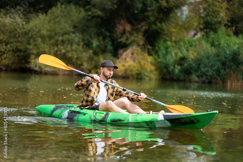 Bearded caucasian man in shirt and cap kayaking at the river. The concept of water sport and canoeing