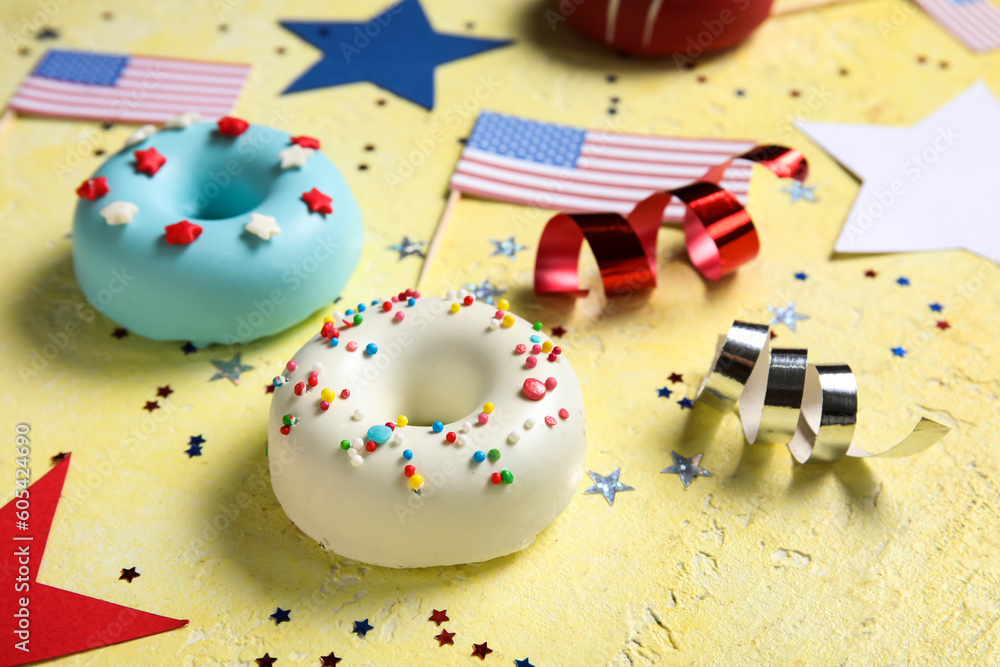 Composition with donuts, USA flags and confetti on yellow table. Independence Day celebration