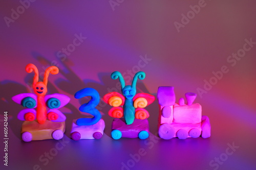 Toy train made of plasticine with butterflies and the number 3. Birthday. A festive event. Color background.