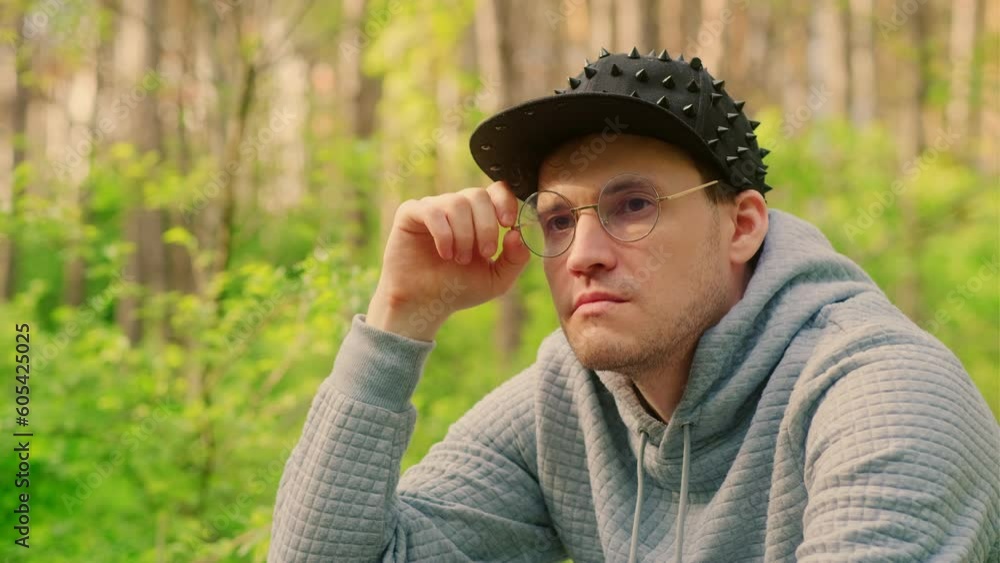 Man in glasses, cap thoughtfully looking away on blurry forest background.
Man in glasses, cap thoughtfully looking away on blurry forest background.