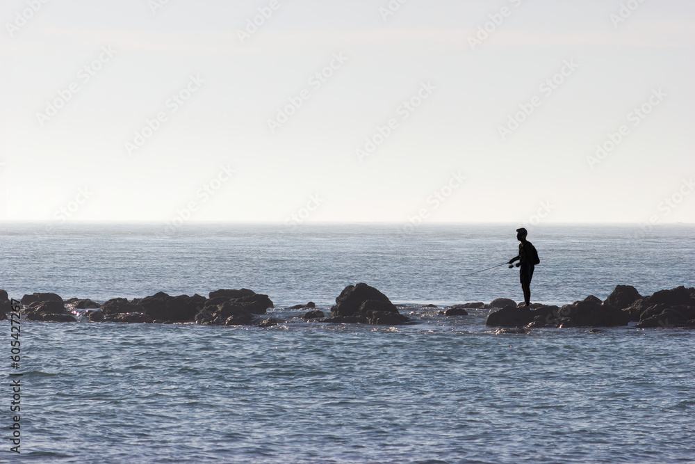 Silhouette of a young man practicing fishing on a breakwater in the sea. Concept of relaxation, sport, fun.