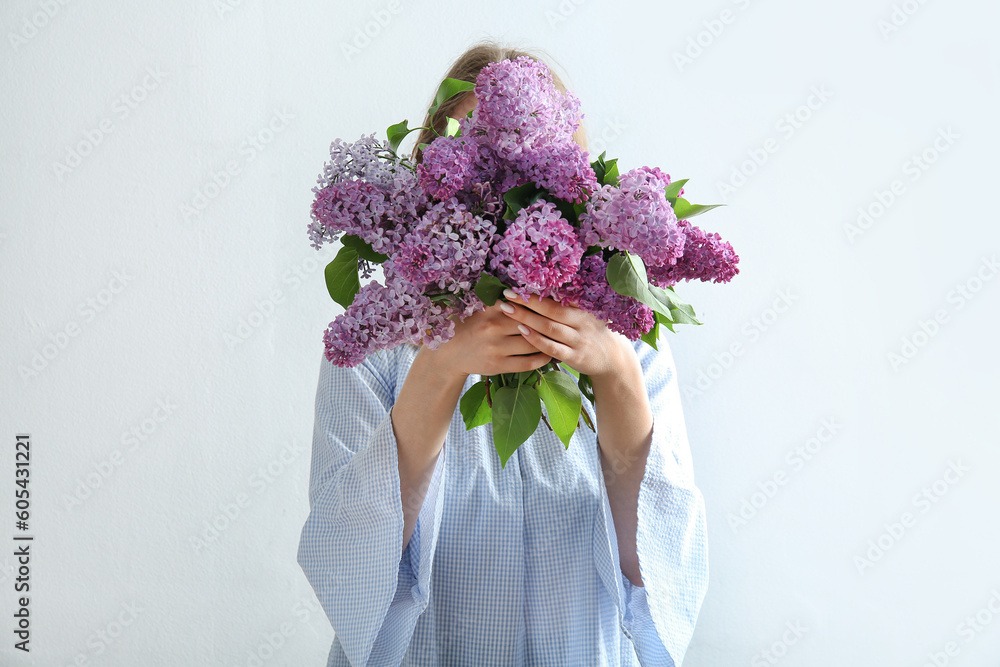 Young woman holding bouquet of beautiful lilac flowers near white wall - obrazy, fototapety, plakaty 