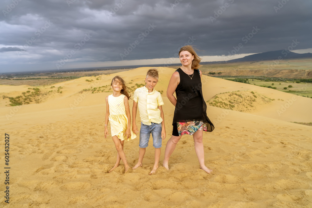 Cheerful mom, son and daughter are standing toghether at desert sand dune in mountains. Fun happy lifestyle summer vacation Cheerful mom, son and daughter are standing toghether at desert sand dune in mountains. Fun happy lifestyle summer vacation