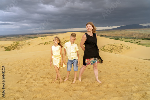 Cheerful mom, son and daughter are standing toghether at desert sand dune in mountains. Fun happy lifestyle summer vacation