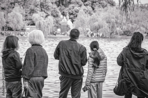 Unidentified family in the park at the edge of a lake. Back view with many people. Black and white street photography
